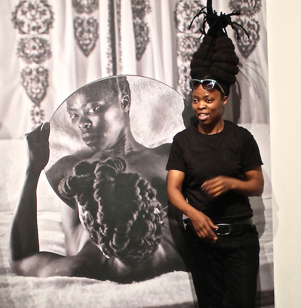 Artist and activist Zanele Muholi poses next to one of her self-portraits in the series Somnyama Ngonyama ("Hail the dark lioness"), which takes up a subset of the Personae exhibition at the Freedom Center.