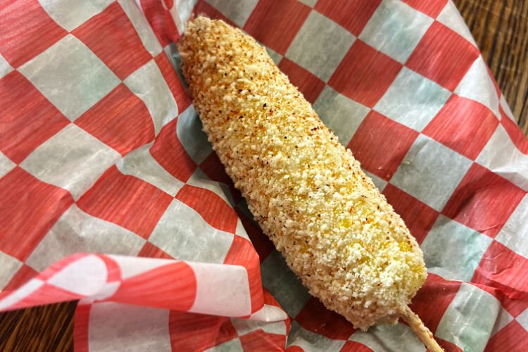 Lita's Tacos street corn specialty: a half cobb of corn speared with a stick for handling, swirled in finely grated cotija cheese with the end rimmed with chili powder.