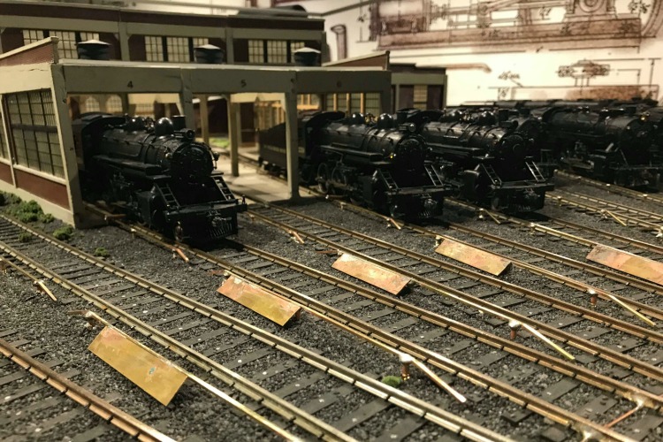 Little locomotives wait on tracks in their own small station.